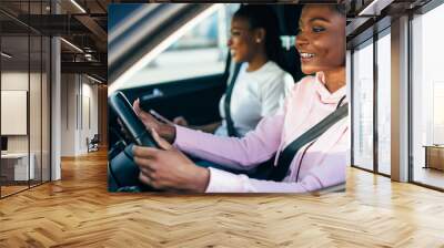 Two beautiful and pretty african women driving in car of their dream.  Two women smiling because of successful purchase of automobile in car dealership. Wall mural